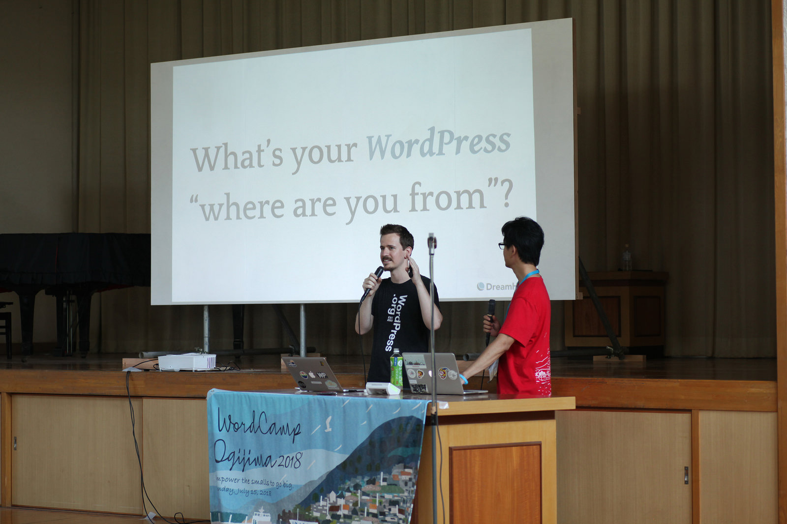 What's your WordPress "where are you from?" と映し出されたスクリーンの前で話をするアメリカ人男性と通訳の西川。